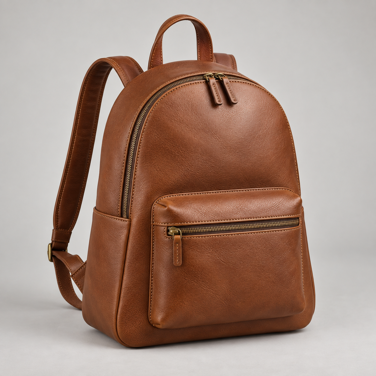 Cognac Daypack: Rounded daypack silhouette with a front zip pocket, short top handle and twin shoulder straps. Illustrative design reference.