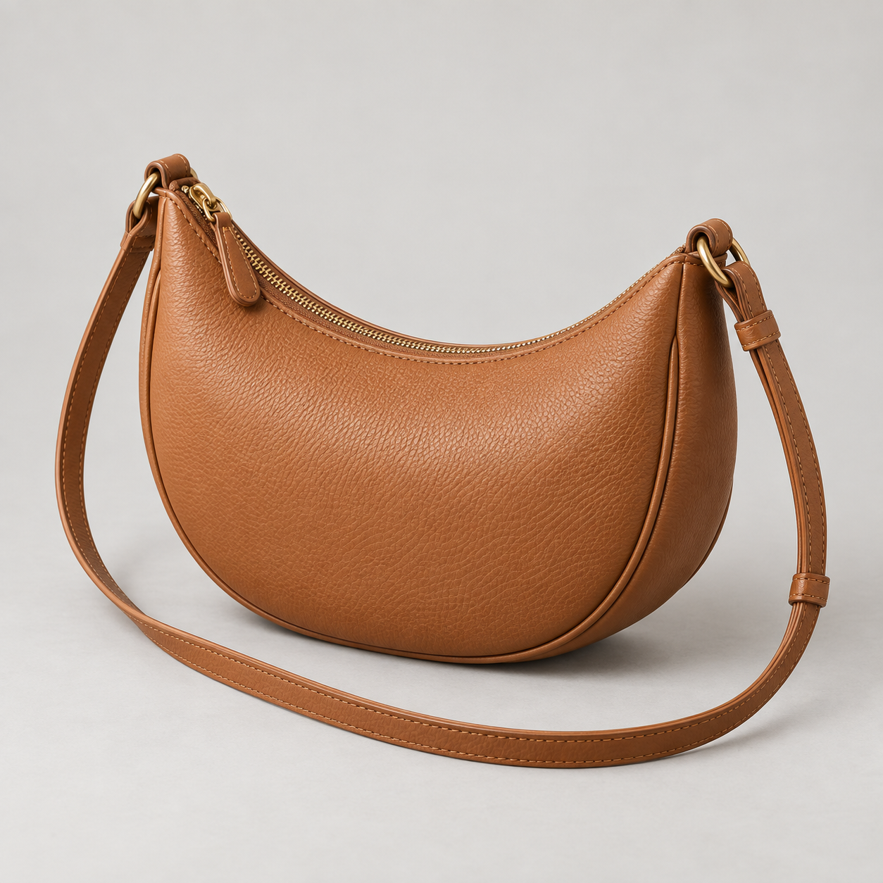 Tan Crescent: Compact crescent crossbody with a curved zip top and a long narrow strap. Illustrative design reference.
